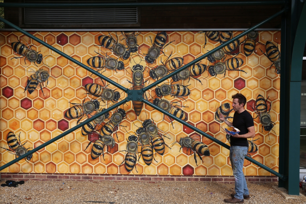 U.S. artist Matthew Willey poses by a mural of bees at Pipers Corner School in the south-east English county of Buckinghamshire, part of his Good of the Hive project to hand-paint 50,000 bees on buildings around the world, October 1, 2020. Photo taken Oct