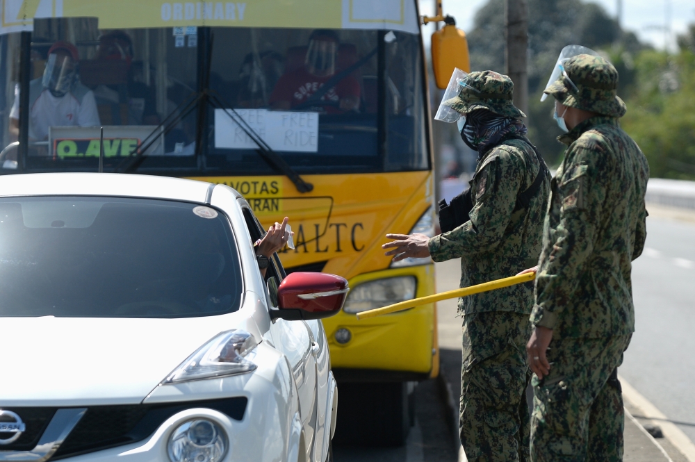 Police officers check an ID of a motorist passing a checkpoint as the country's capital returns to stricter lockdown measures amid rising coronavirus disease (COVID-19) cases, in Quezon City, Metro Manila, Philippines, March 29, 2021. REUTERS/Lisa Marie D