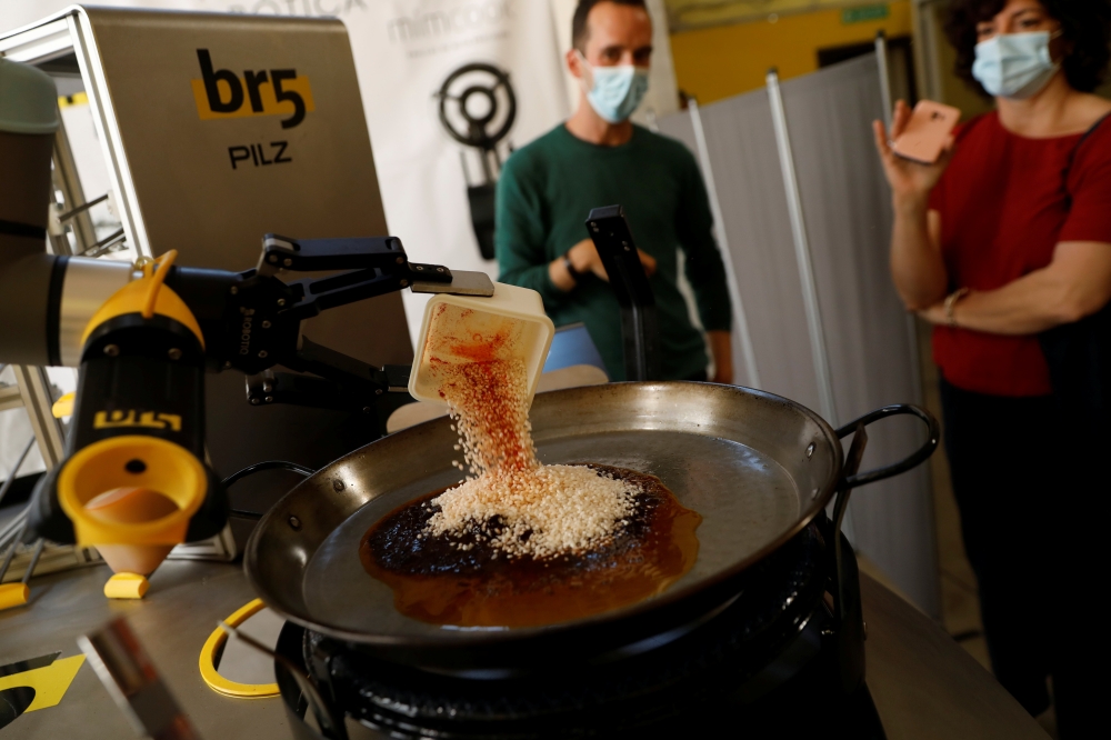 Chef Maria Munoz watches as a robot created by Spanish companies br5 and Mimcook makes paella during a demonstration at a warehouse in San Fernando de Henares, outside Madrid, Spain, May 20, 2021. Picture taken May 20, 2021. (REUTERS/Susana Vera)