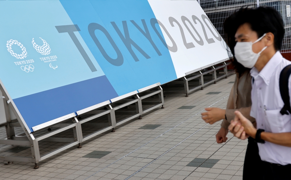 People walk past a sign for the 2020 Tokyo Olympic Games that have been postponed to 2021 due to the coronavirus disease (COVID-19) pandemic, at the IBC/MPC media center at Tokyo Big Sight exhibition center in Tokyo, Japan June 30, 2021. REUTERS/Fabrizio 