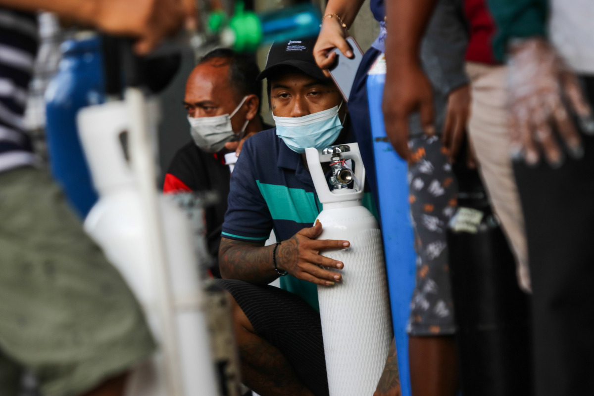 Men wearing protective face masks wait outside a store with their oxygen cylinders to get them refilled, amid a surge of coronavirus disease (COVID-19) cases, in Surabaya, East Java Province, Indonesia July 12, 2021, in this photo taken by Antara Foto. Di