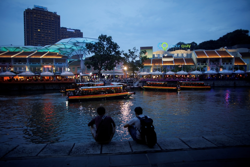 People sit on the banks of the Singapore River at Clarke Quay in Singapore April 14, 2018. REUTERS/Thomas White/File Photo
