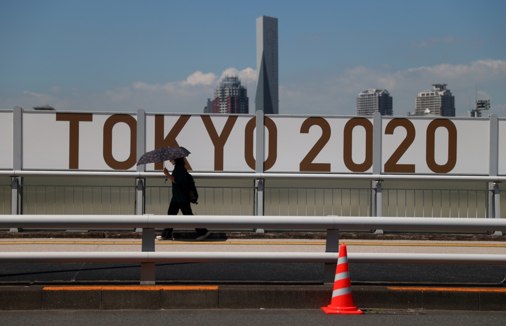 July 19, 2021 A woman shelters from the sun under an umbrella as she walks past Olympics signage REUTERS/Thomas Peter/File Photo