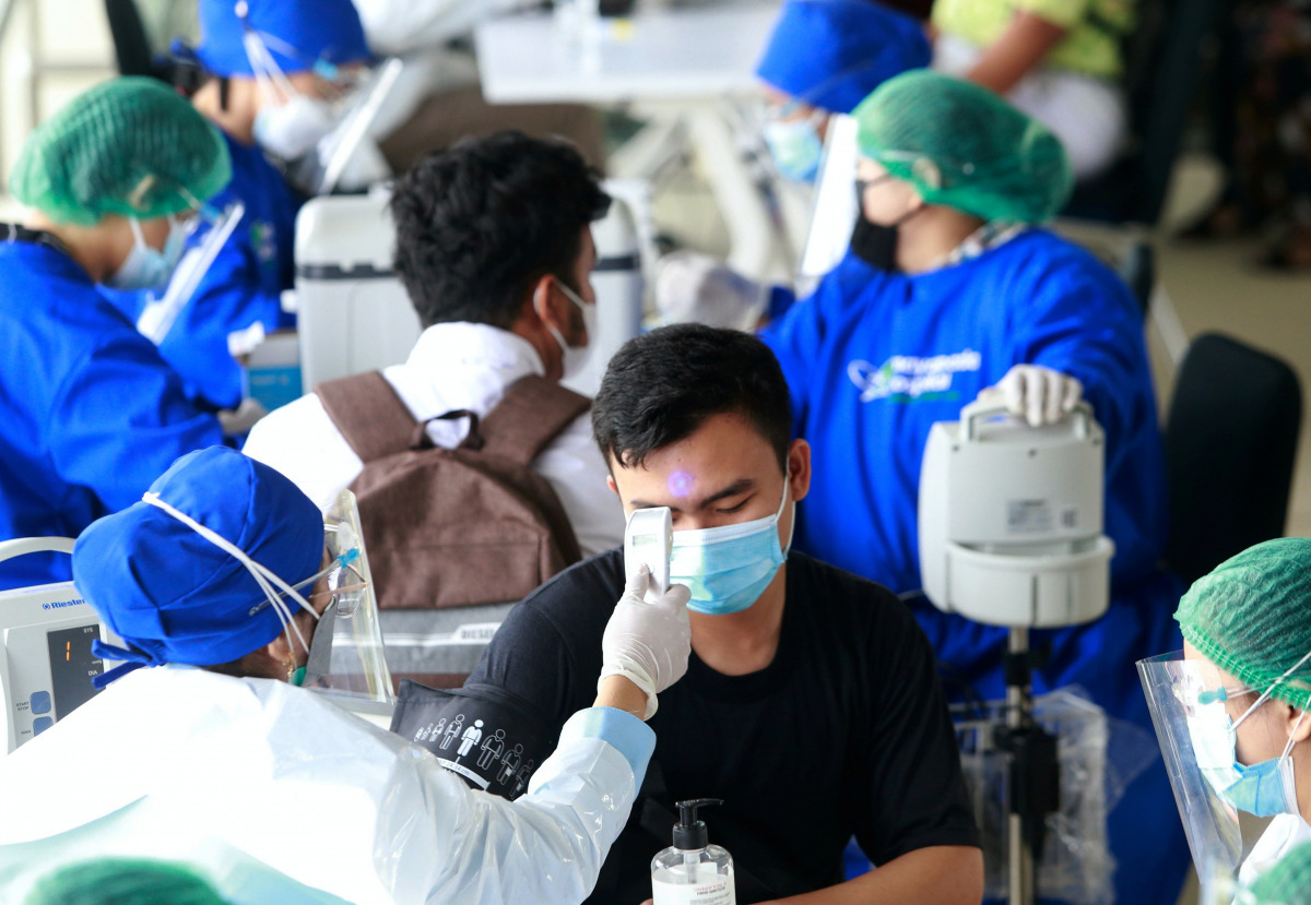  A healthcare worker in personal protective equipment (PPE) checks a man's temperature with a thermal scanner before he receives a dose of the vaccine against the coronavirus disease (COVID-19) at a Mass Rapid Transit (MRT) station, as cases surge in Jaka