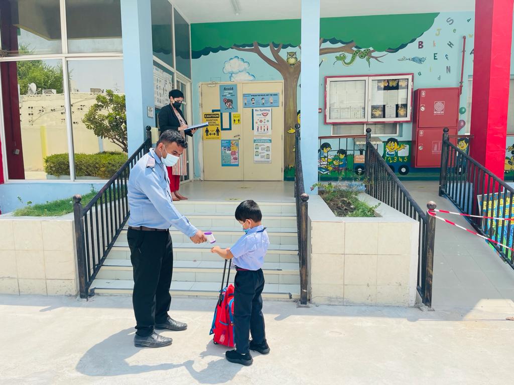 A security personnel checking the temperature of a student at school entrance.