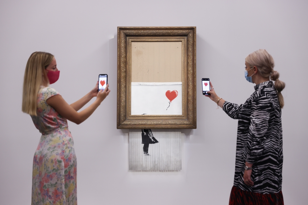 A gallery assistant poses by 'Love is in the Bin', an artwork by Banksy, which will be for sale in an auction, at Sotheby's in London, Britain, September 3, 2021. Reuters/Tom Nicholson
