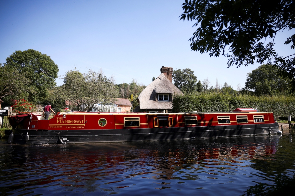 Pianist Masayuki Tayama steers his canal boat concert hall, named The Piano Boat, along the Colne Valley Canal in Harefield, Britain, September 8, 2021. Picture taken September 8, 2021. REUTERS/Henry Nicholls
 
