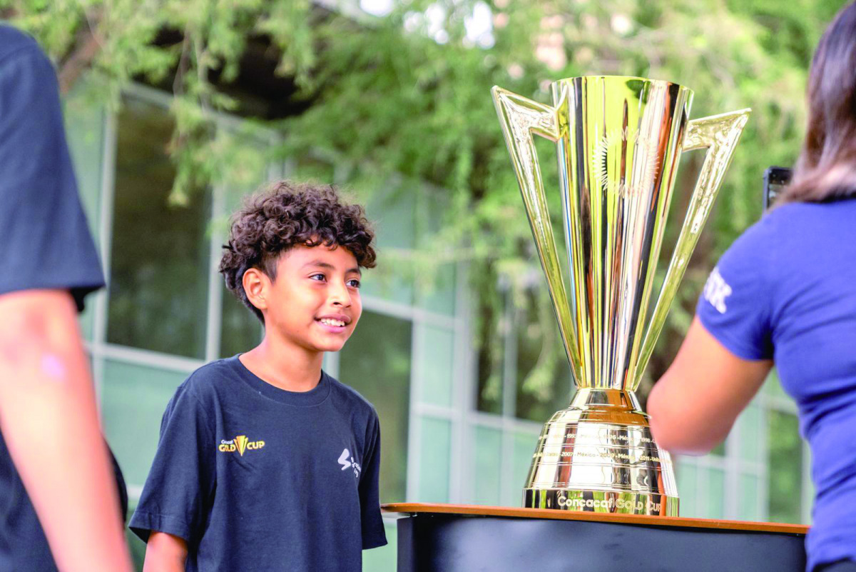A young football fan posing for a photograph with the CONCACAF Champions' Trophy.