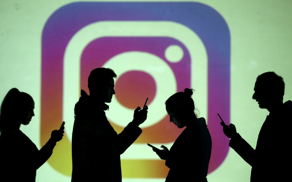 FILE PHOTO: Silhouettes of mobile users are seen next to a screen projection of Instagram logo in this picture illustration taken March 28, 2018. REUTERS/Dado Ruvic/Illustration