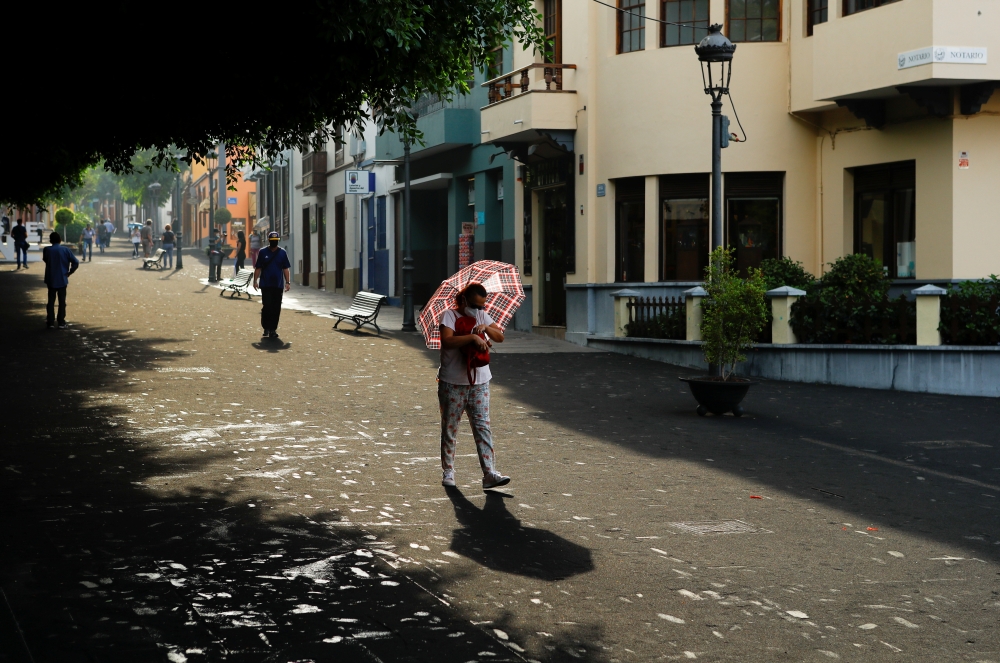 A woman walks with an umbrella to protect herself from the falling ash following the eruption of a volcano on the Canary Island of La Palma, in Los Llanos de Aridane, Spain, October 1, 2021. REUTERS/Borja Suarez