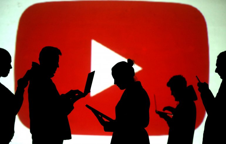 FILE PHOTO: Silhouettes of laptop and mobile device users are seen next to a screen projection of the YouTube logo in this picture illustration taken March 28, 2018. REUTERS/Dado Ruvic/Illustration/File Photo