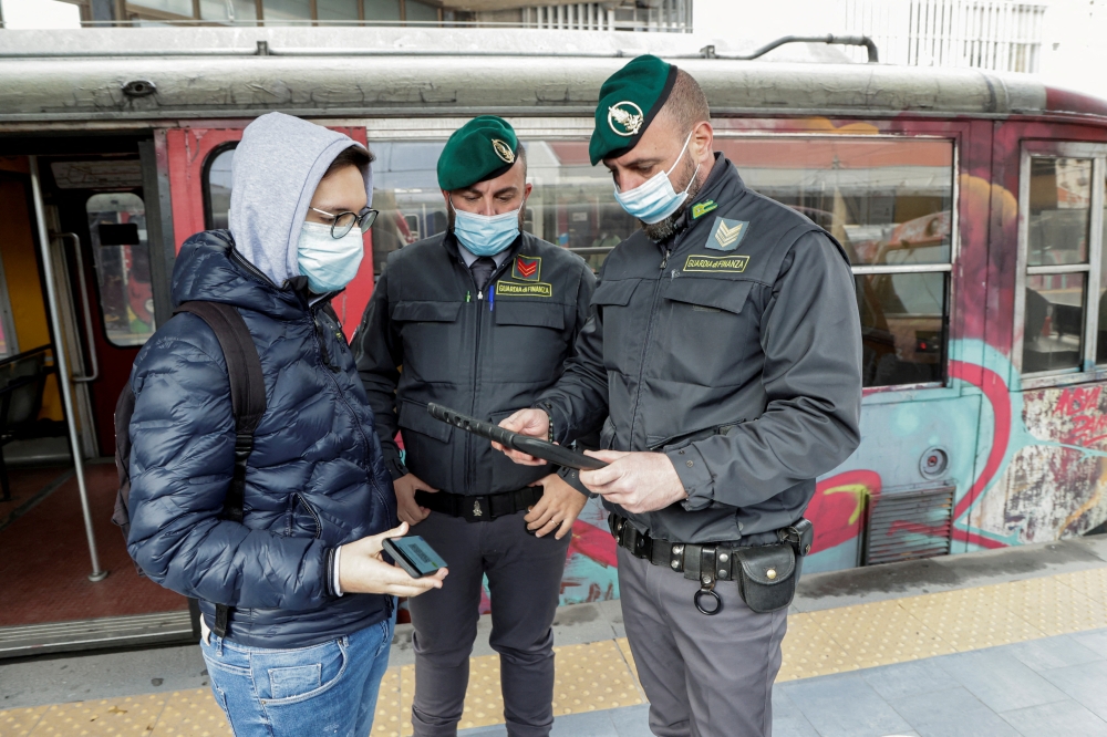 Guardia di Finanza officers check the coronavirus disease (COVID-19) health pass, known as a Green Pass, of a person at a train station the day the government restricts access of unvaccinated, in Naples, Italy December 6, 2021. REUTERS/Ciro de Luca/File Photo
