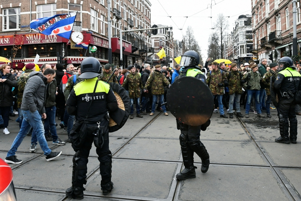Police officers stand guard as opponents of restrictions imposed in the Netherlands to contain the spread of the coronavirus disease (COVID-19) protest despite a ban by local authorities, in Amsterdam, Netherlands, January 2, 2022. REUTERS/Piroschka van de Wouw
