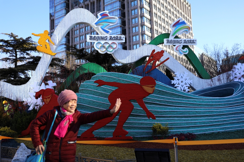 A woman poses for pictures in front of an installation featuring National Speed Skating Oval and logos of the Beijing 2022 Winter Olympics, in Beijing, China January 17, 2022. REUTERS/Tingshu Wang