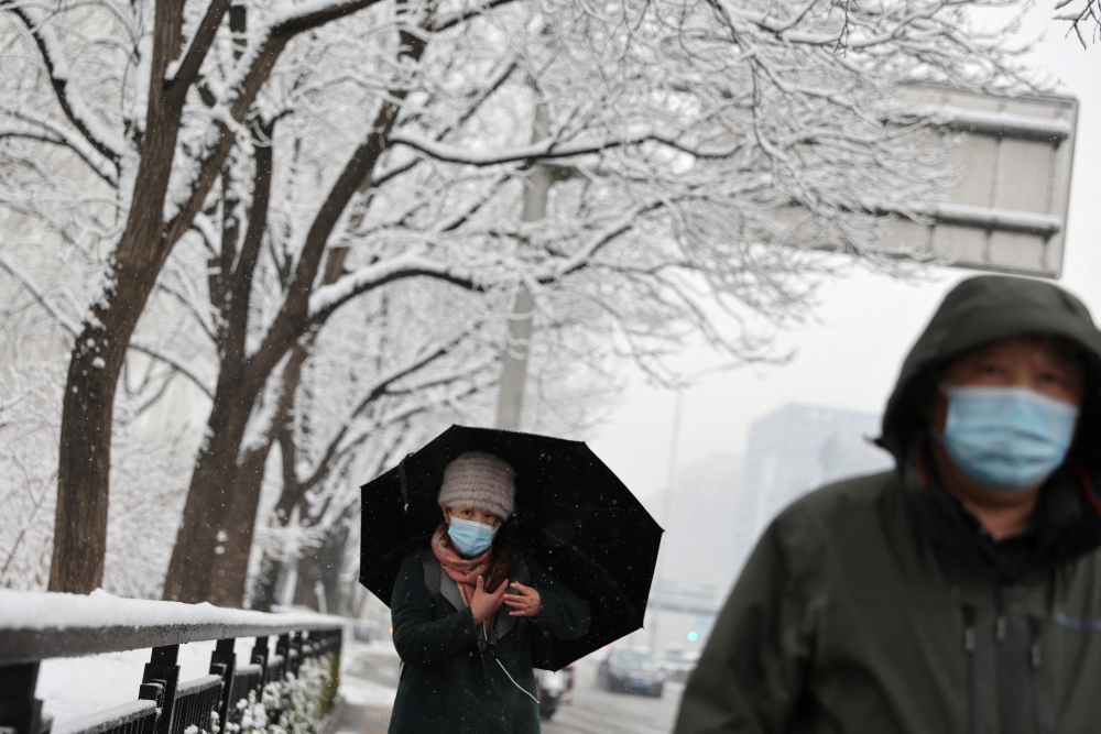 People wearing face masks to prevent the spread of the coronavirus disease (COVID-19), walk on the street amid snowfall in Beijing, China March 18, 2022. REUTERS/Tingshu Wang