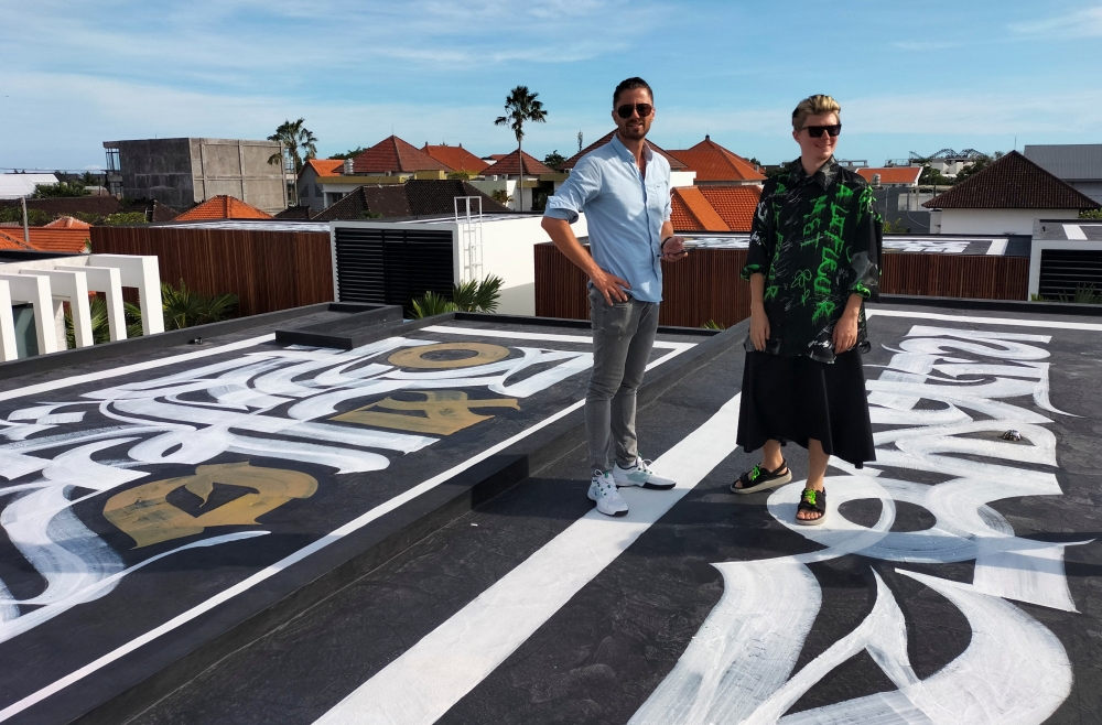 Russian artist Pokras Lampas and Ukrainian Alex Shtefan pose with one of nine of Pokras' calligraphy artwork on the rooftop of Alex's villas in Bali, Indonesia on March 16, 2022. REUTERS/Sultan Anshori