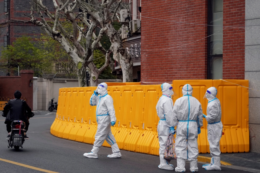 Workers in protective suits stand next to a sealed-off area before the second stage of a two-stage lockdown to curb the spread of the coronavirus disease (COVID-19), in Shanghai, China March 31, 2022. REUTERS/Aly Song