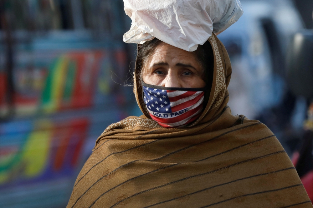 A woman wears a mask to prevent contracting the coronavirus disease (COVID-19) as she carries a bag of supplies on her head in Karachi, Pakistan, January 26, 2022. REUTERS/Akhtar Soomro