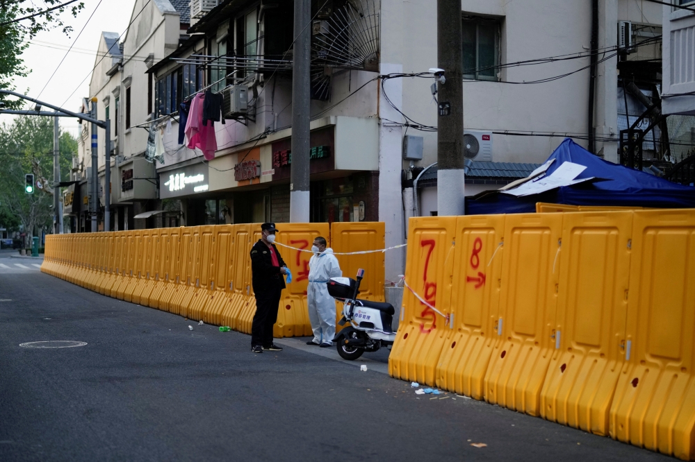 A worker in a protective suit keeps watch next to barricades set around a sealed-off area, during a lockdown to curb the spread of the coronavirus disease (COVID-19) in Shanghai, China April 11, 2022. Reuters/Aly Song