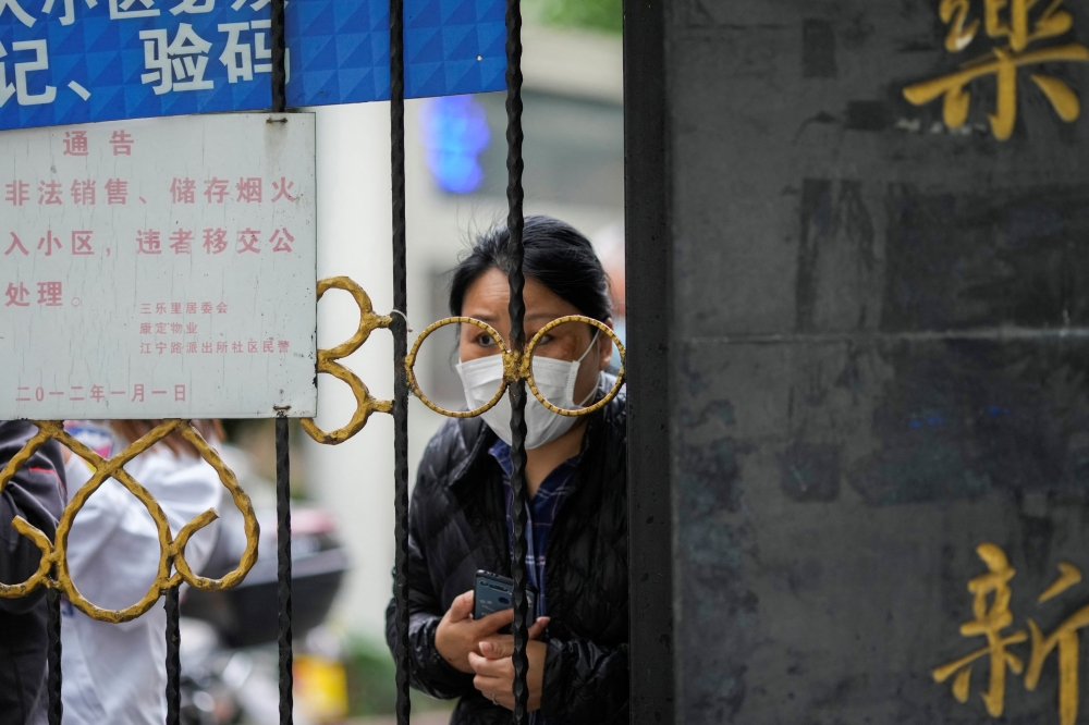 A resident waiting for a food delivery looks out from behind a gate blocking an entrance to a residential area under lockdown amid the coronavirus disease (COVID-19) pandemic, in Shanghai, China REUTERS/Aly Song