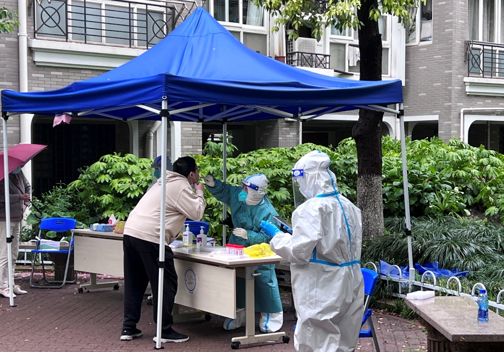 A medical worker in a protective suit collects a swab from a resident at a makeshift nucleic acid testing site inside a residential compound under lockdown in Shanghai, China April 14, 2022. Reuters/Xihao Jiang
