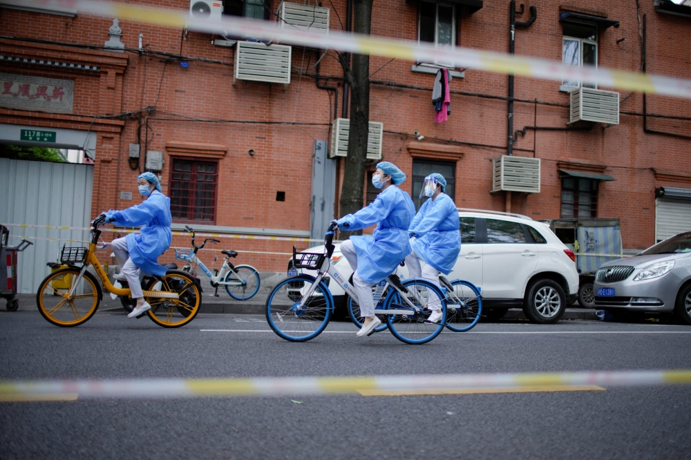 Workers in protective suits ride bicycles of bike-sharing service on a street during lockdown amid the coronavirus disease (COVID-19) pandemic, in Shanghai, China, April 15, 2022. REUTERS/Aly Song