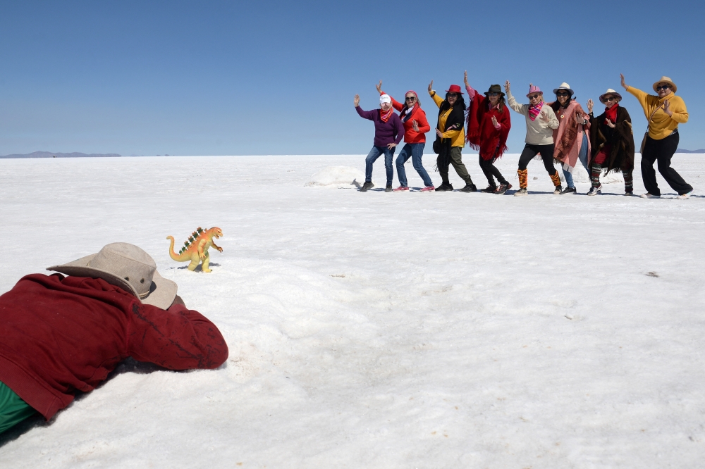 A boy takes photos of tourists behind a toy dinosaur for a fee, at the Uyuni Salt Flat in Bolivia March 27, 2022. Picture taken March 27, 2022. REUTERS/Claudia Morales