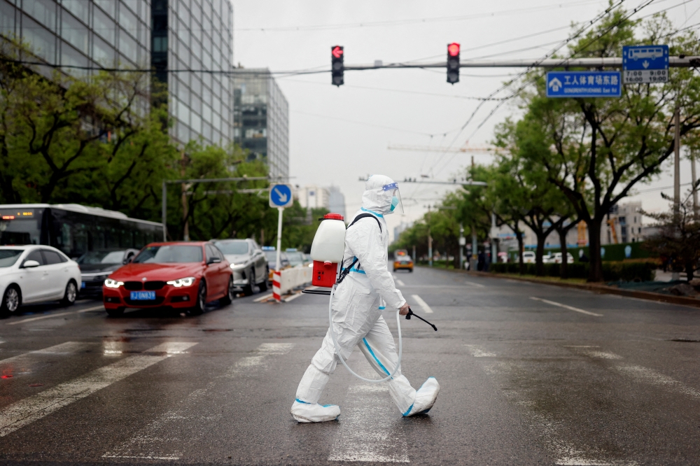 A worker wearing a protective suit and carrying disinfection equipment crosses a road amid the coronavirus disease (COVID-19) outbreak in Beijing, China April 27, 2022. REUTERS/Carlos Garcia Rawlins/File Photo
