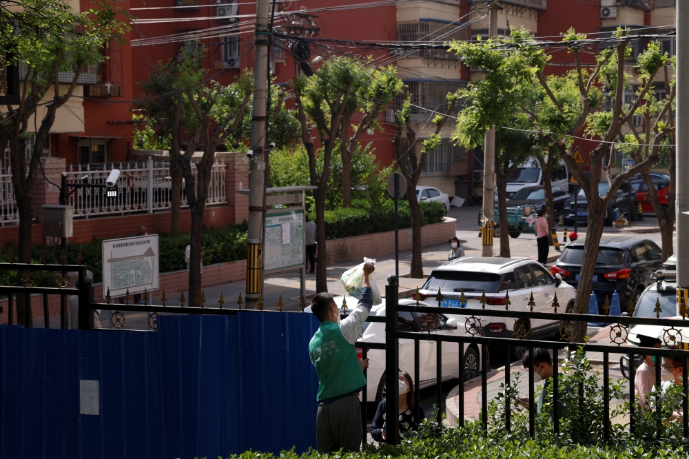 A courier makes a delivery over a fence of a residential area under lockdown, amid the coronavirus disease (COVID-19) outbreak in Beijing, China, May 4, 2022. REUTERS/Carlos Garcia Rawlins
