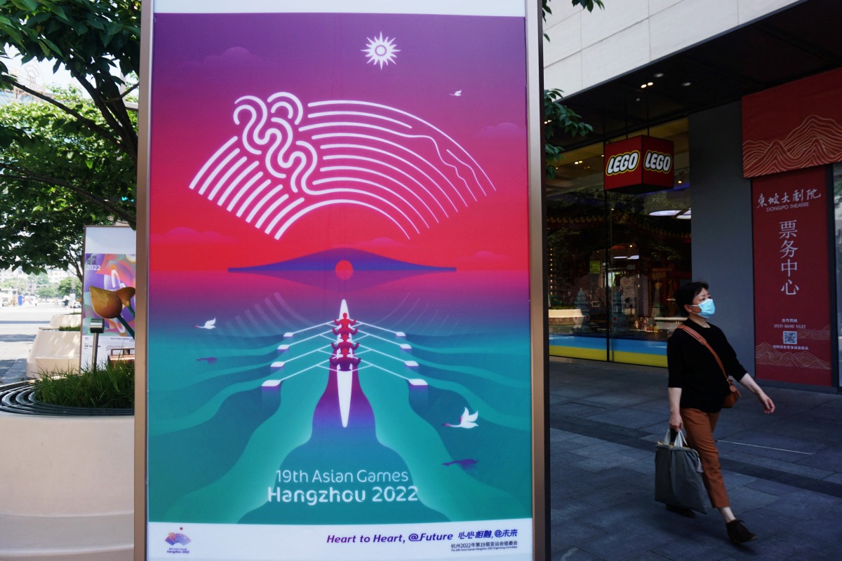 A person wearing a protective mask walks past a billboard for the 19th Asian Games Hangzhou 2022, amid the coronavirus disease (COVID-19) outbreak, in Hangzhou, Zhejiang province, China May 6, 2022. China Daily via REUTERS 