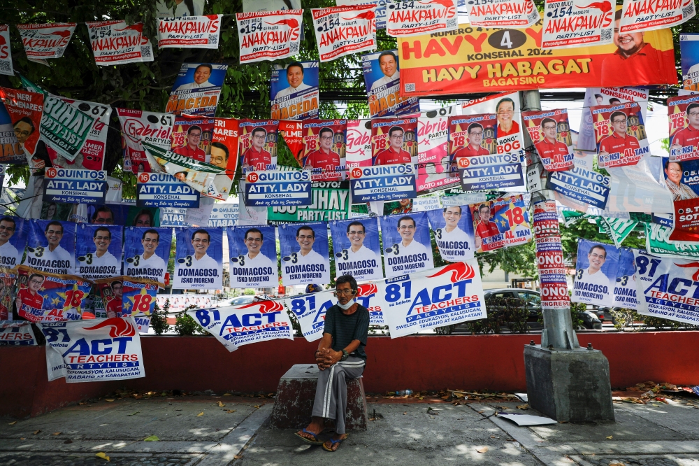 A man sits below election posters a day prior to the national elections in Manila, Philippines, May 8, 2022. REUTERS/Willy Kurniawan