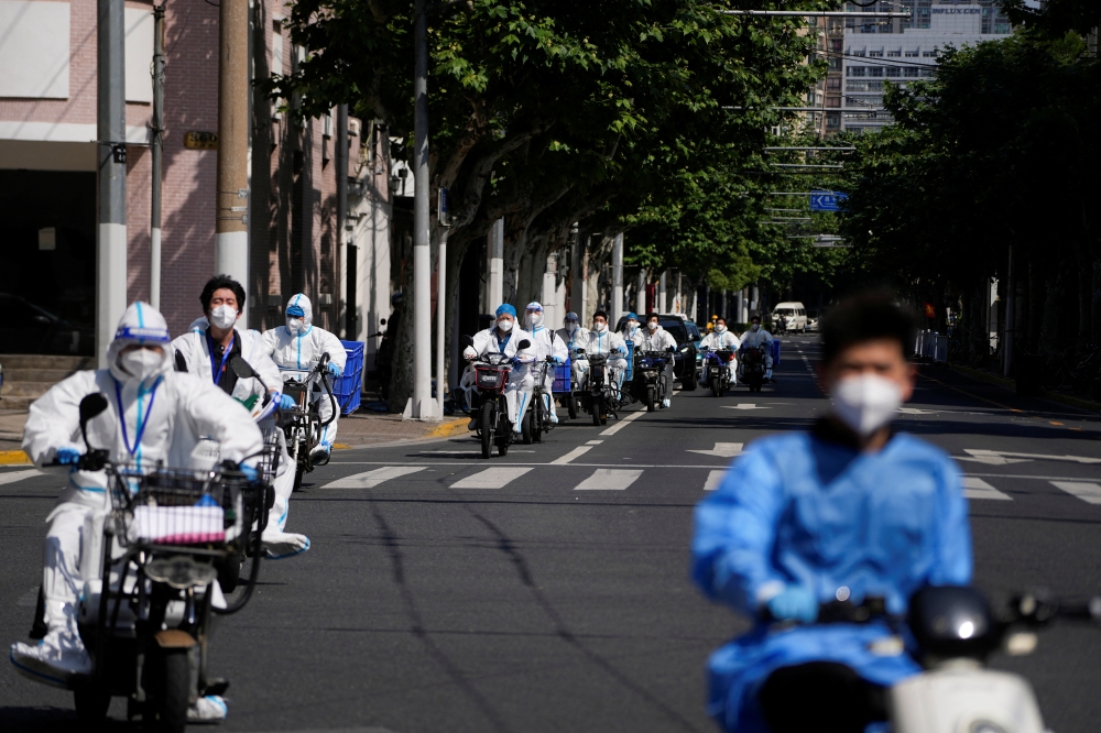 Workers in protective suits ride electric scooters across the street during lockdown, amid the coronavirus disease (COVID-19) pandemic, in Shanghai, China, May 18, 2022. REUTERS/Aly Song