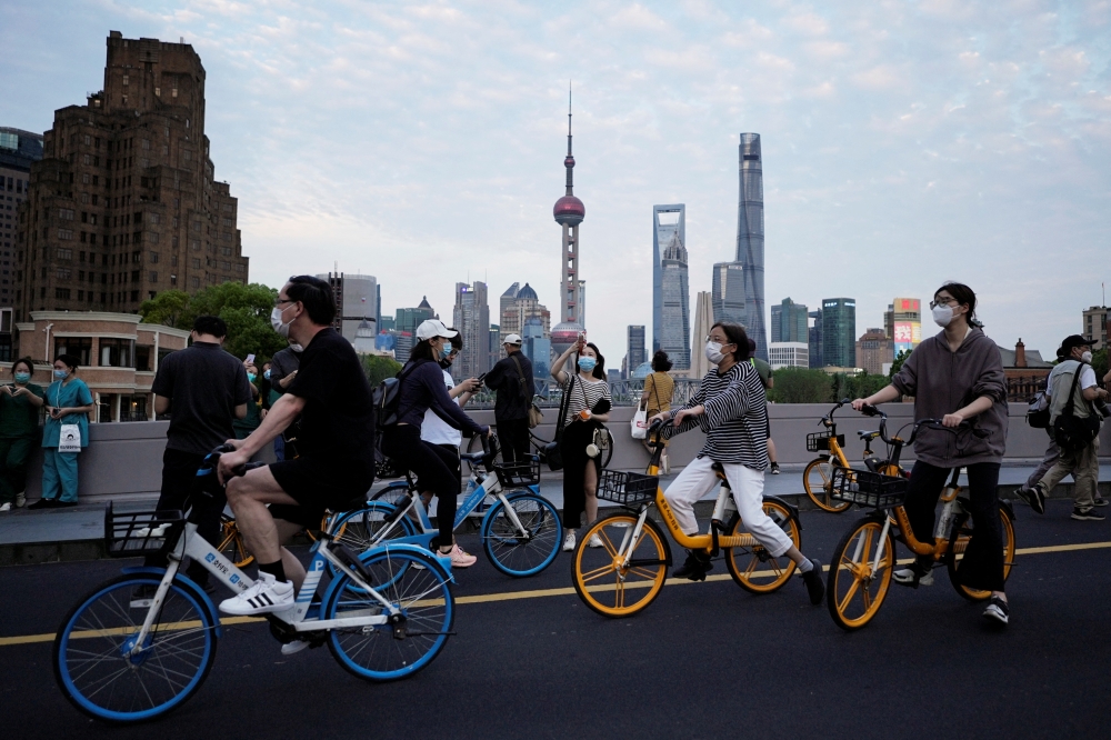 A woman wearing a protective face mask holds up her mobile phone as she stands near cyclists passing by on a bridge in Shanghai, China May 31, 2022. Reuters/Aly Song
 