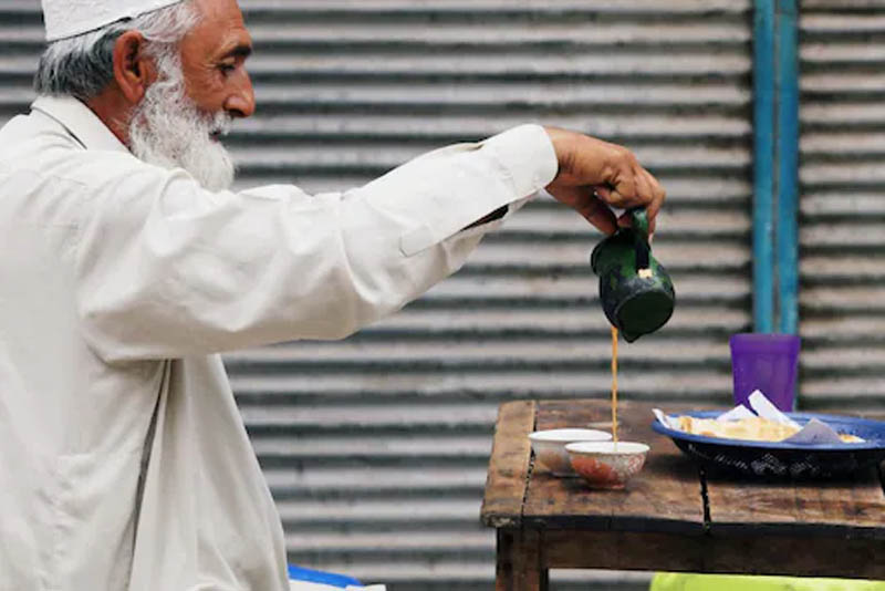FILE PHOTO: A man fills a cup of tea while having breakfast with paratha flatbread, outside closed shops in Peshawar, Pakistan July 18, 2018. REUTERS/Fayaz Aziz
