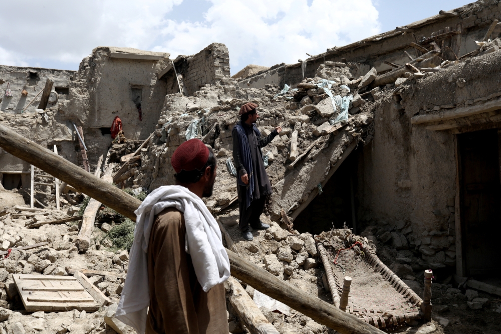 Afghan men stand on the debris of a house that was destroyed by an earthquake in Gayan, Afghanistan, June 23, 2022. (REUTERS/Ali Khara)