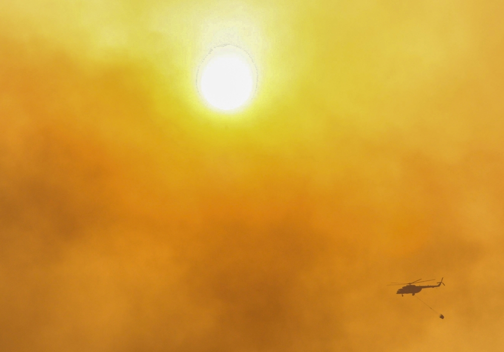 A firefighting helicopter flies through the smoke that raises from wildfires during a sunset near Marmaris, a town in Mugla province, Turkey, June 23, 2022. (REUTERS/Kenan Gurbuz)