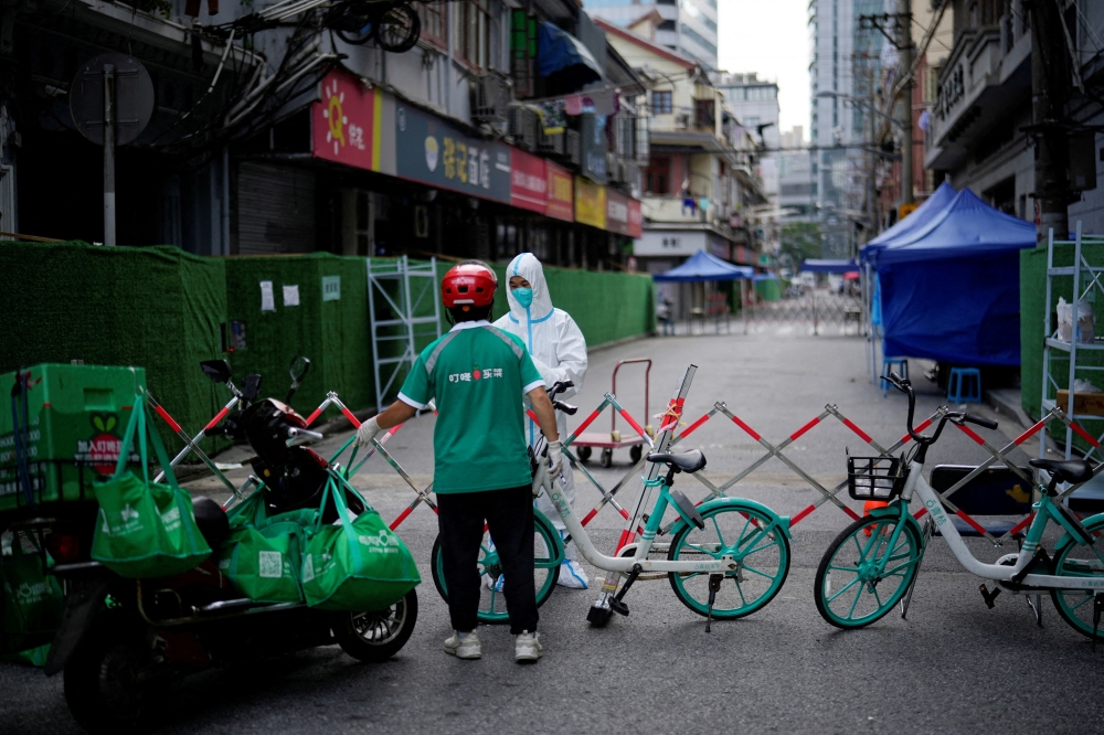 FILE PHOTO: A worker in a protective suit gets food from a delivery worker at a closed residential area during lockdown, amid the coronavirus disease (COVID-19) outbreak, in Shanghai, China, May 25, 2022. REUTERS/Aly Song
