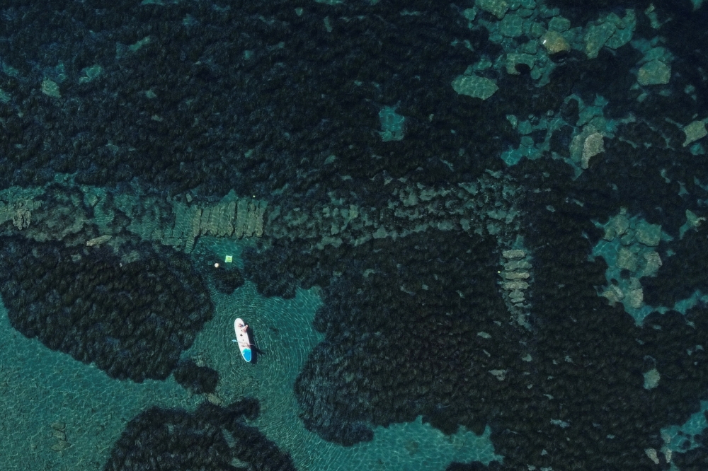 Visitors paddle on a stand up paddle board (SUP) at the underwater archaeological park of the ancient port of Amathus in Limassol, Cyprus July 9, 2022. REUTERS/Yiannis Kourtoglou