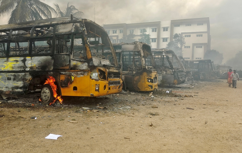 People walk past damaged school buses that were set on fire by a mob in the school campus after a female student's death in Kallakurichi district in the southern state of Tamil Nadu, India, July 17, 2022. (REUTERS)