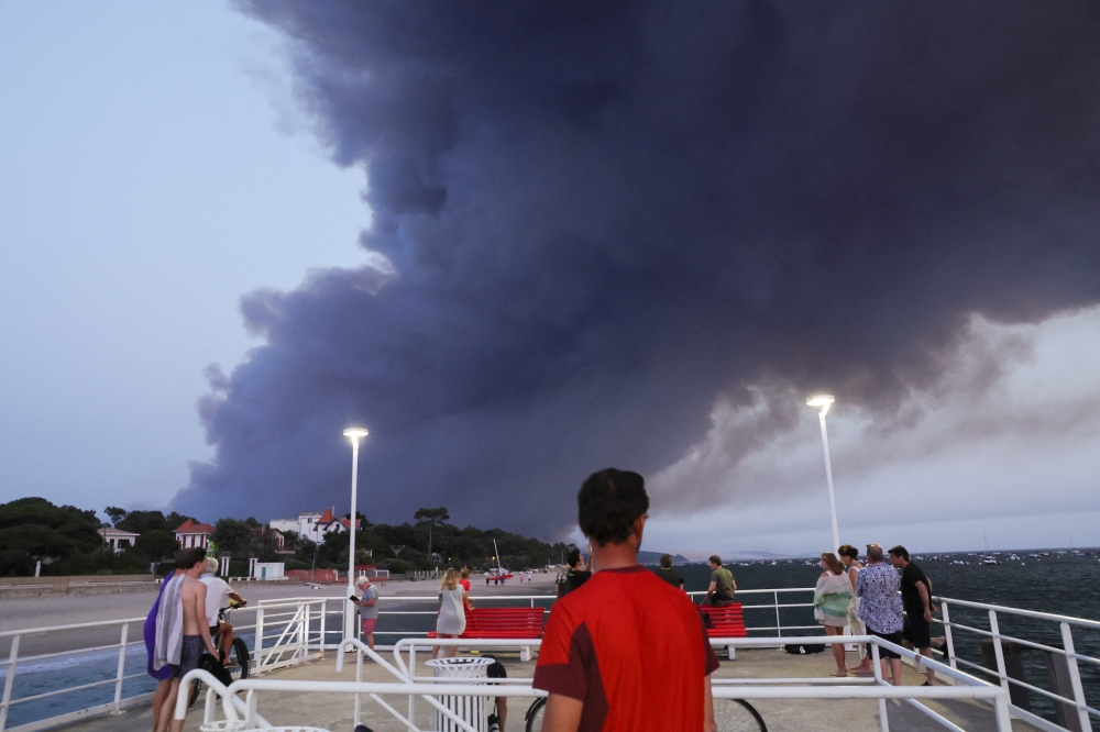 Beachgoers react, as smoke produced by wildfires in La Teste-de-Buch forest billows, Arcachon, France, July 18, 2022. REUTERS/Pascal Rossignol