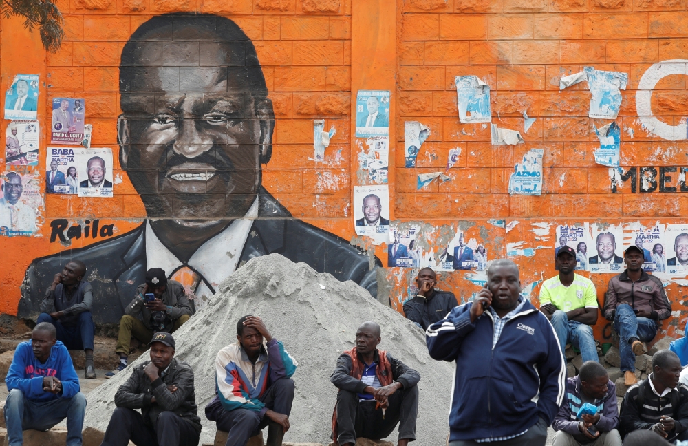 People sit next to a wall mural of Raila Odinga the presidential candidate for Azimio la Umoja and One Kenya Alliance in Kibera slums of Nairobi, Kenya August 12, 2022. Reuters/Monicah Mwangi