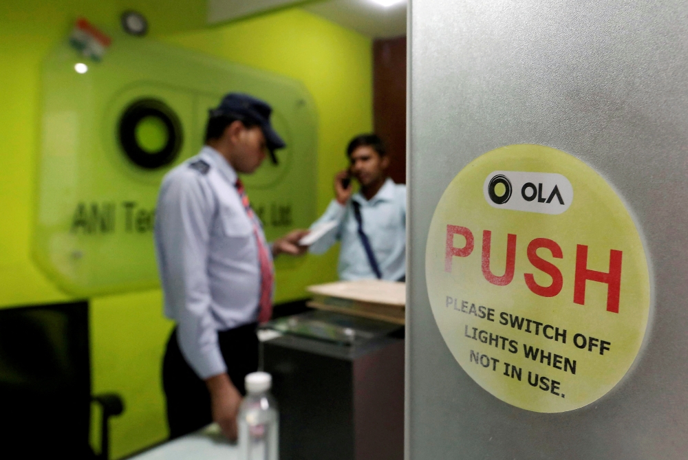 An employee speaks over his phone as a private security guard looks on at the front desk inside the office of Ola cab service in Gurugram, April 20, 2016. Reuters/Anindito Mukherjee/File Photo
