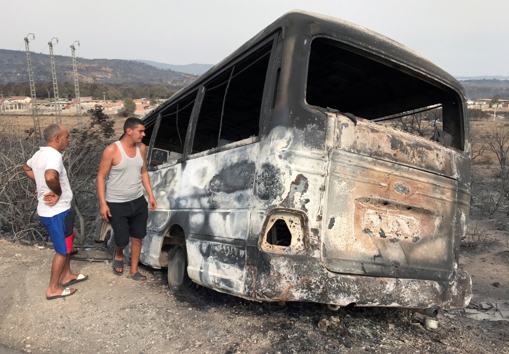 Men inspect a bus that was burnt following a wildfire in El Kala, in Al Tarf province, Algeria August 18, 2022. REUTERS/Ramzi Boudina