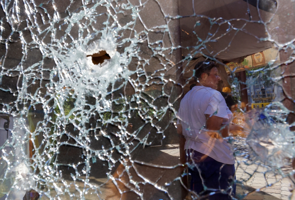 A woman stands behind a broken window of the hotel Central, which was damaged by recent shelling in the course of Ukraine-Russia conflict in Donetsk, Ukraine, August 23, 2022. (REUTERS/Alexander Ermochenko)