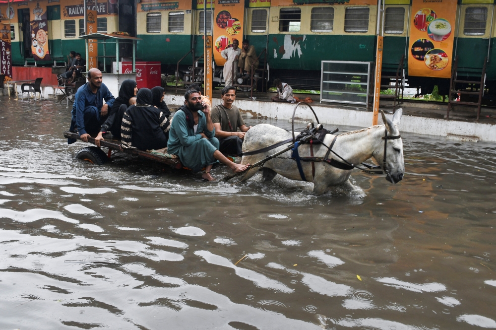People ride on a donkey cart along a flooded road, following rains during the monsoon season in Hyderabad, Pakistan, August 24, 2022. (REUTERS/Yasir Rajput) 