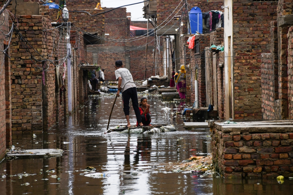 A man and a girl use a makeshift raft as they cross a flooded street, following rains during the monsoon season in Hyderabad, Pakistan, August 24, 2022. (REUTERS/Yasir Rajput)

