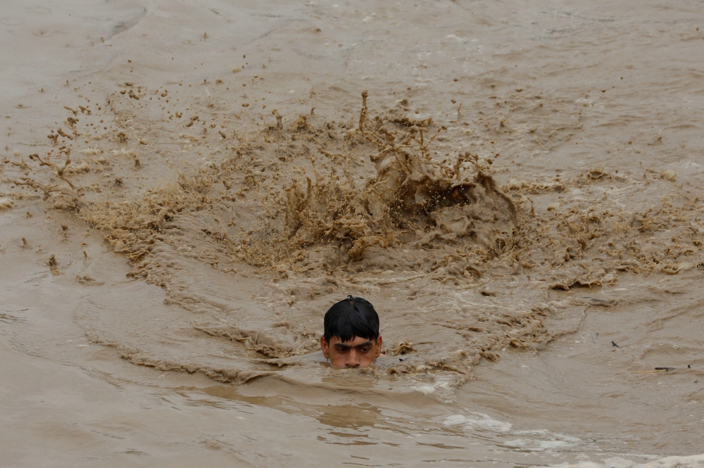 A man swims in flood waters while heading for a higher ground, following rains and floods during the monsoon season in Charsadda, Pakistan August 27, 2022. REUTERS/Fayaz Aziz