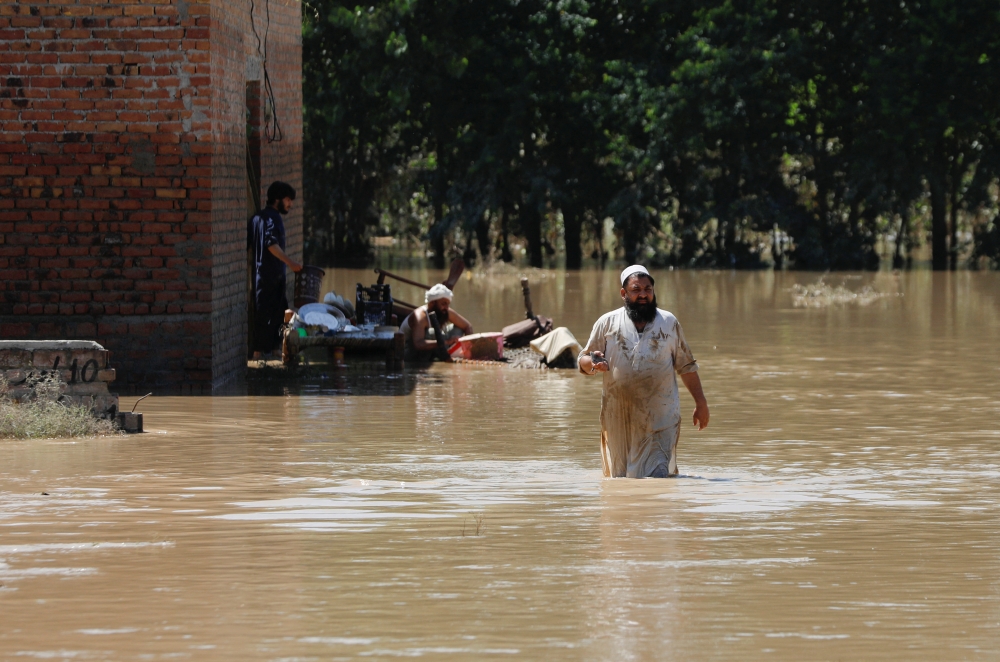 A man wades through flood waters trying to salvage his belongings following rains and floods during the monsoon season in Charsadda, Pakistan August 28, 2022. REUTERS/Fayaz Aziz