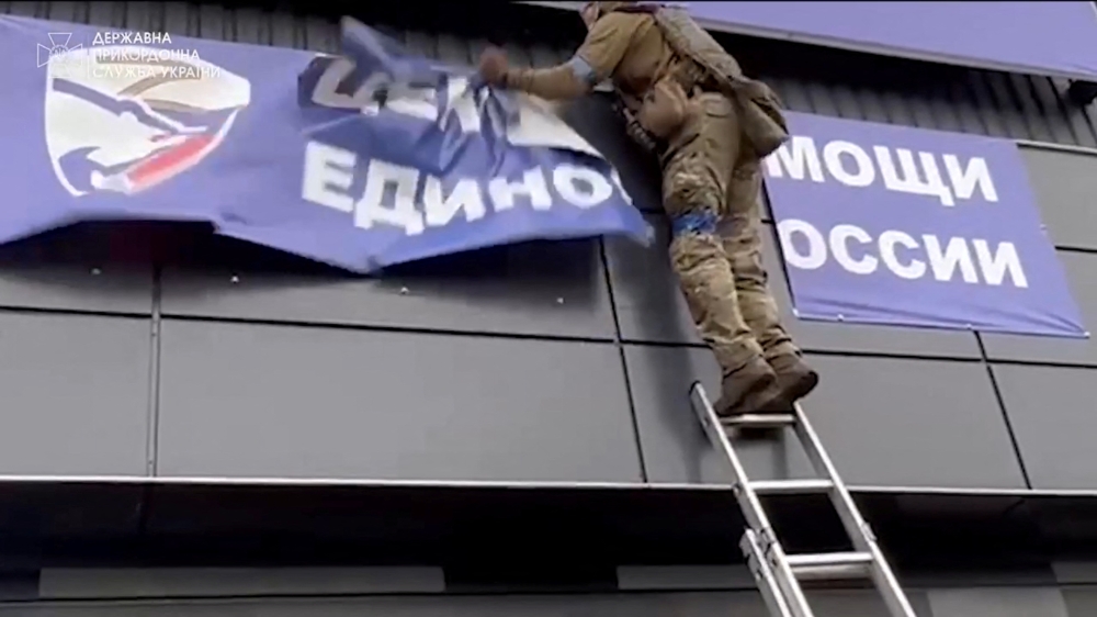 A Ukrainian soldier rips down a banner, amid Russia's invasion of Ukraine, in Vovchansk, Ukraine in this image from a video released September 13, 2022. State Border Service of Ukraine/Handout via REUTERS