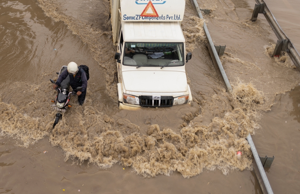 A man pushes his stalled motorbike on a flooded street as a truck drives past after heavy rains in Gurugram, on the outskirts of New Delhi, India, September 23, 2022. Reuters/Adnan Abidi